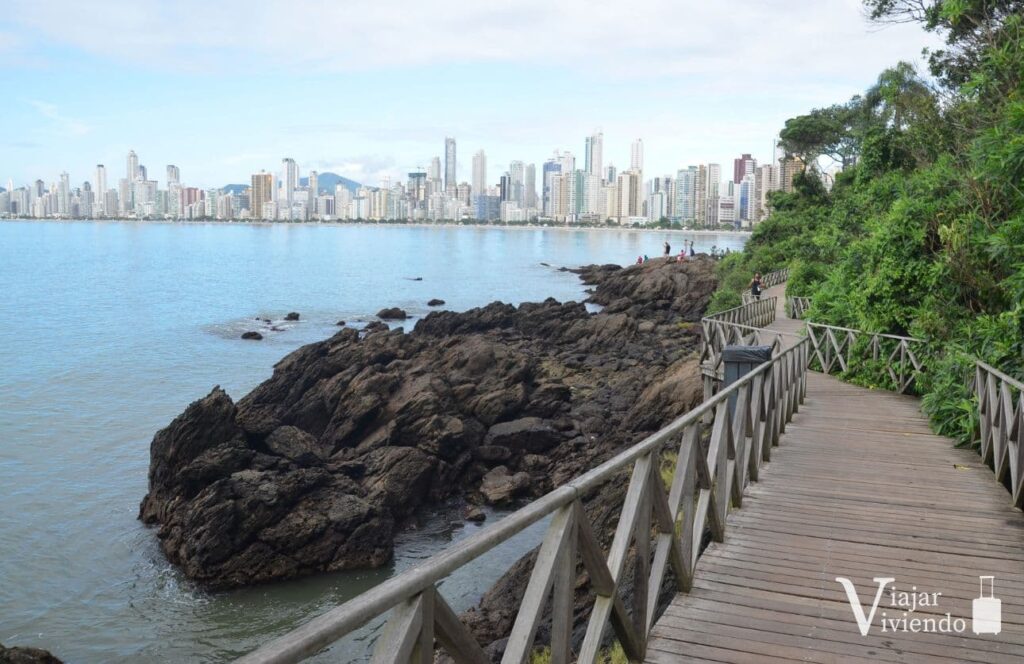 pasarela de madera que conduce a la playa de buraco junto al mar con la los edificios del balneario de camboriu de fondo